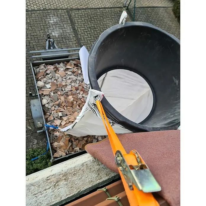 Stortslurf Trichter - Durchmesser: 50 cm - Aufnahme von einem Dachdecker-Eimer, der mit einem Spanngurt gesichert ist, mit Bauschutt in einem Anhänger darunter.