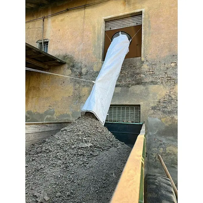 Stortslurf Schuttrutsche - Ø x L: 50 x 300 cm - Eine Vorrichtung leitet Erde durch ein Fenster in einen Anhänger, um das Abladen zu erleichtern. Praktische Lösung für schwere Materialien.