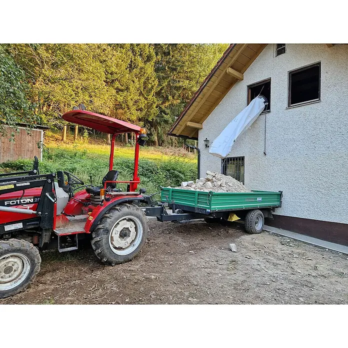 Stortslurf Schuttrutsche - Ø x L: 50 x 300 cm - Ein roter Foton 254 Traktor zieht einen grünen Anhänger, der mit Bauschutt gefüllt ist, unter einem Fenster mit Bauschuttrutsche.