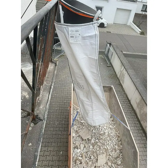 Stortslurf Schuttrutsche - Ø x L: 50 x 300 cm - Das Bild zeigt einen Big Bag, der mit Bauschutt gefüllt ist. Der Big Bag hängt an einem Geländer und entleert sich in einen Container.