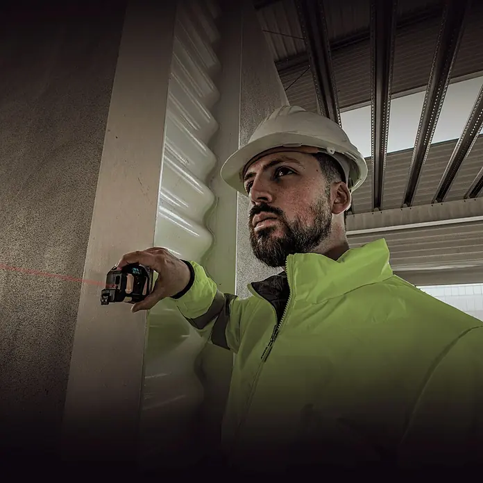 Vito Cinta métrica extensible VIFMML40 - Largo: 5 m - Un trabajador de la construcción utiliza un medidor láser y lleva un casco para garantizar mediciones precisas.