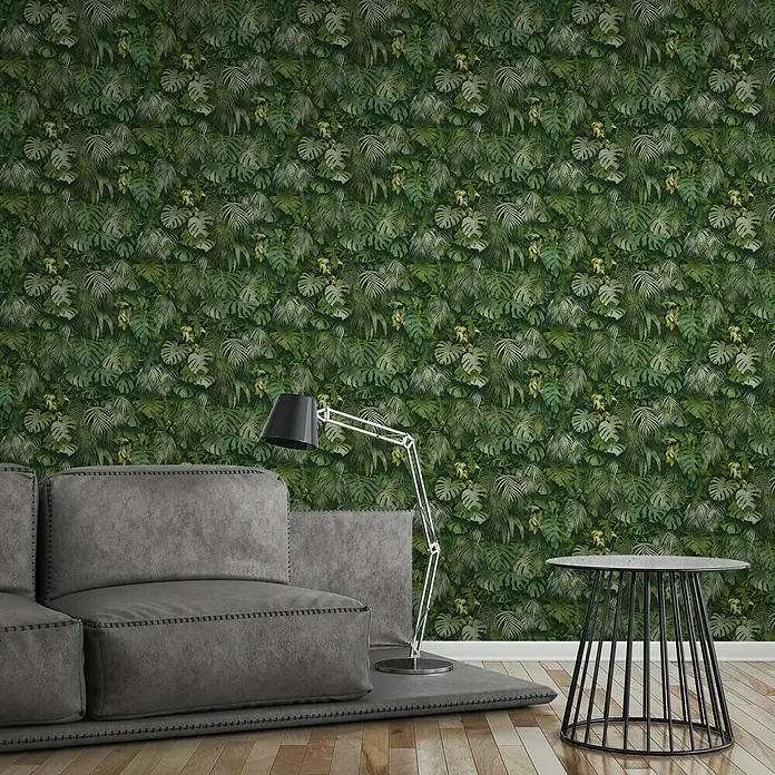 A.S. Création Greenery Vliestapete Dschungelblätter - Grün, Floral, 10,05 x 0,53 m - Wohnzimmer mit grauer Couch, Stehlampe und Beistelltisch vor einer grünen Blättertapete.