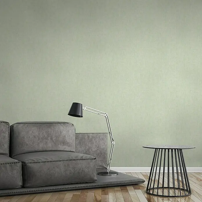 A.S. Création Greenery Vliestapete Strukturuni - Hellgrün, Uni, 10,05 x 0,53 m - Ein stilvolles Interieur mit einem grauen modularen Sofa und einem modernen Beistelltisch neben einer eleganten Lampe.