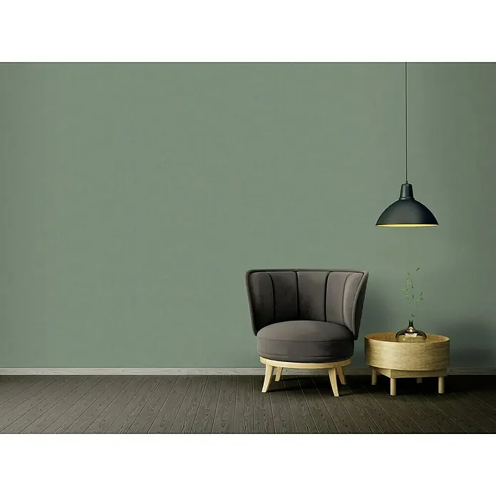 A.S. Création Ethnic Origin Vliestapete - Grün, Uni, 10,05 x 0,53 m - Elegantes Interieur mit grauem Sessel, Beistelltisch und Pendelleuchte vor einer olivgrünen Wand. Stilvolles Ambiente für modernes Wohnen.