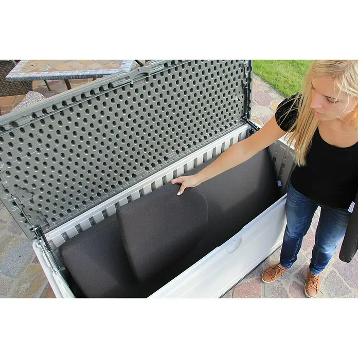Lifetime Gartenbox XXL - L x B x H: 153 x 61 x 66 cm, Kunststoff - Frau verstaut Kissen in einer großen, wetterfesten Aufbewahrungsbox für den Außenbereich, ideal für Gartenmöbel und Polster.