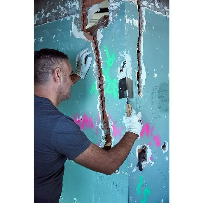 Bellota Espátula para ángulos exteriores - Angular - Un hombre trabaja en una pared con ladrillos a la vista, sujetando una herramienta, posiblemente renovando o reparando la estructura.