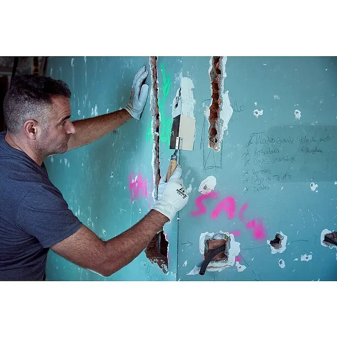 Bellota Espátula para ángulos exteriores - Angular - Un manitas con espátula y guantes trabaja en una pared azul con huecos y anotaciones.