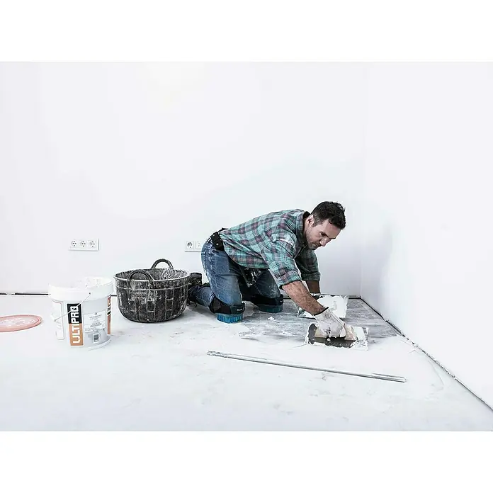 Bellota Llana de alisado recta 5816-2 - 160 x 300 mm - Un hombre está aplicando pavimento con una llana en una habitación. Un cubo y otras herramientas están listos.
