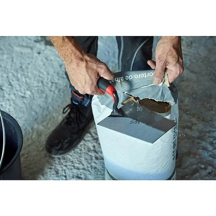 Bellota Paleta de albañil TRF44BM - 130 x 175 mm, Acero - Primer plano de un hombre usando una llana para abrir un saco de mortero blanco, una herramienta esencial para proyectos de construcción.