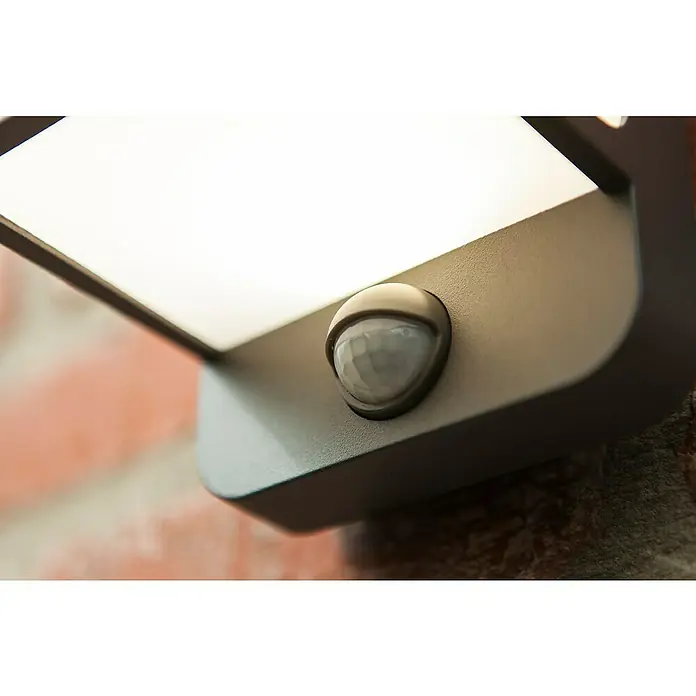 Lutec Doblo LED-Sensor-Außenwandleuchte - 14 W, L x B x H: 10,3 x 11 x 146 cm, Anthrazit - Nahaufnahme einer modernen Außenleuchte mit Bewegungsmelder an einer Ziegelmauer. Stilvolles Design trifft auf Funktionalität.
