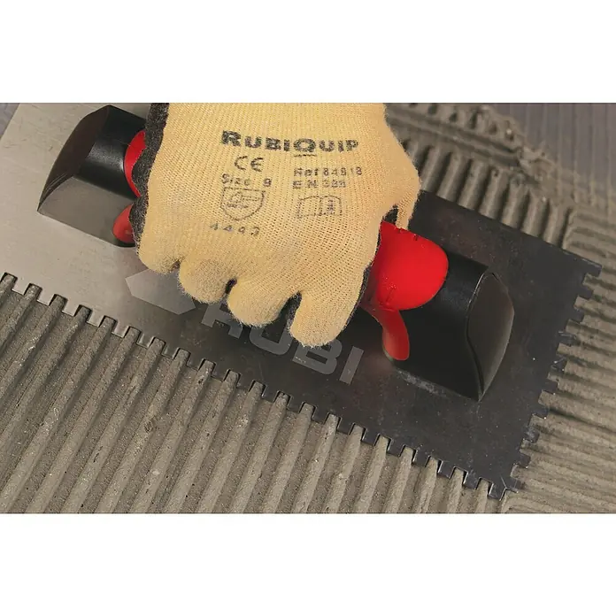 Rubi Llana dentada Rubiflex - 120 x 280 mm, Dientes 10x10, Mango bimaterial - Primer plano de una mano con guante de trabajo que sostiene una llana dentada RUBI, aplicando mortero adhesivo sobre baldosas.