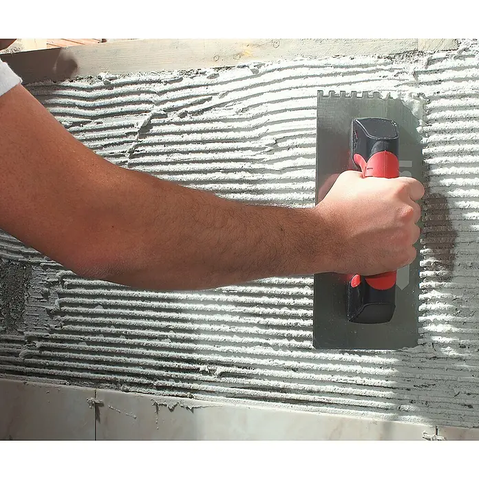 Rubi Llana dentada Rubiflex - 120 x 280 mm, Dientes 6x6, Mango bimaterial - Artesano utiliza llana dentada para aplicar adhesivo para baldosas a una pared. La herramienta es esencial para un trabajo de colocación preciso.