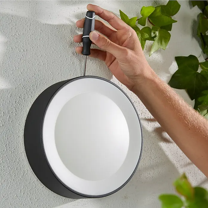 Philips Hue LED-Außenwandleuchte White & Color Ambiance Daylo - 15 W, 22 x 22 x 7,6 cm, Schwarz, IP44 - Nahaufnahme einer runden Wandleuchte in Schwarz-Weiß, die mit einem Schraubenzieher an einer Wand befestigt wird.