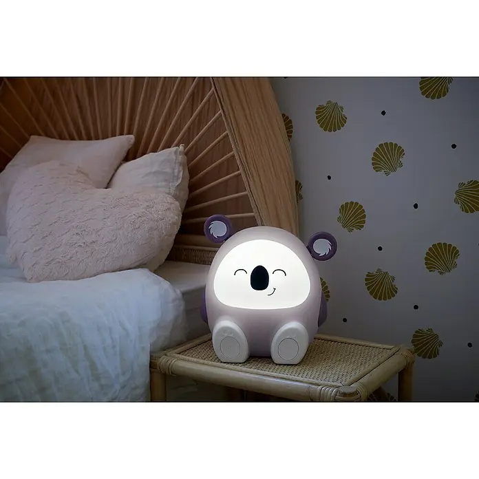 Altavoz Bluetooth Coco Koala - Violeta, 15 W - Linda luz nocturna de koala en una mesita de noche junto a una cama, creando un ambiente cálido y reconfortante para los niños.