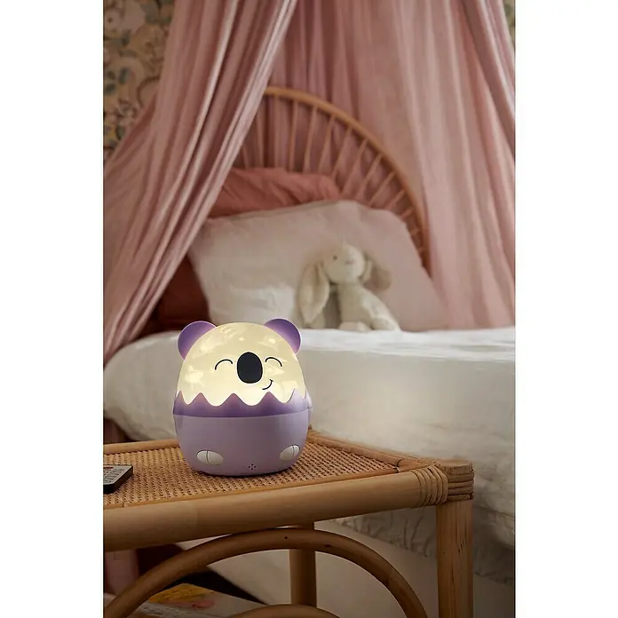 Lámpara de sobremesa LED Coco Koala - Violeta, RGBW - Una linda luz nocturna con forma de koala se sienta en una mesita de noche, perfecta para la habitación de un niño.