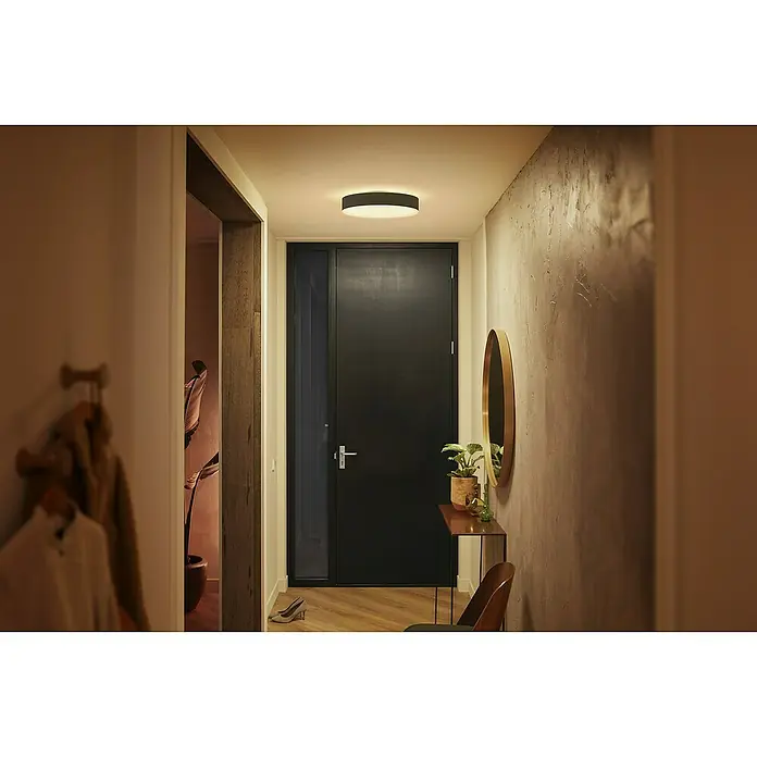 Philips Hue LED-Deckenleuchte rund White Ambience Enrave M - 19 W, Ø x H: 38,1 x 8,4 cm, Schwarz, Kaltweiß - Eine stilvolle Fluransicht mit einer modernen Deckenleuchte, die den Raum hell erleuchtet und einladend wirkt.