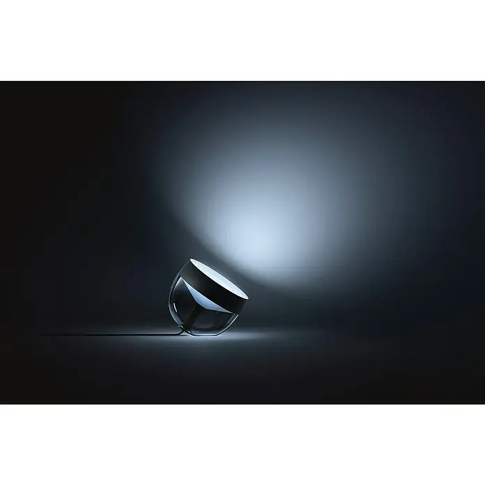 Philips Hue LED-Tischleuchte Iris - Schwarz/Transparent, Höhe: 19,4 cm - Nahaufnahme einer eleganten Tischleuchte, die ein sanftes Licht in einem dunklen Raum verbreitet. Das Lichtdesign ist modern und minimalistisch.
