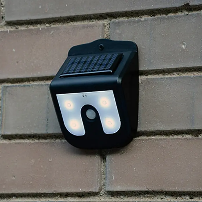 Solar-Außenwandleuchte Vigilamp - 0,8 W, L x B x H: 4,2 x 9,2 x 12,3 cm, Weiß, Schwarz, IP44 - Eine schwarze Solar-Wandleuchte mit vier LED-Leuchten, die an einer Ziegelmauer befestigt ist, sorgt für energieeffiziente Beleuchtung.