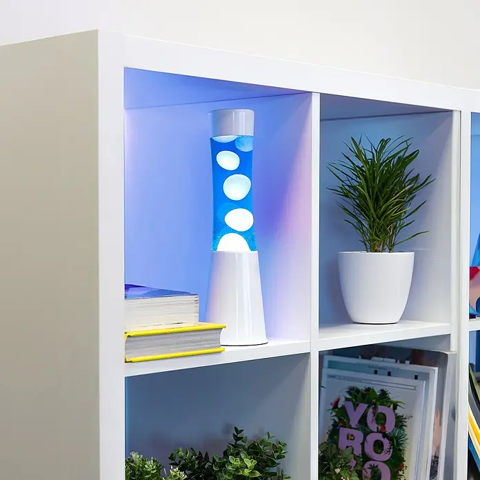 Lámpara de sobremesa decorativa lava mini - 25 W, L x An x Al: 9 x 9 x 30 cm, Blanco, Azul - Una lámpara de lava azul con burbujas de cera blanca está en un estante blanco junto a libros y plantas, creando un ambiente relajante.