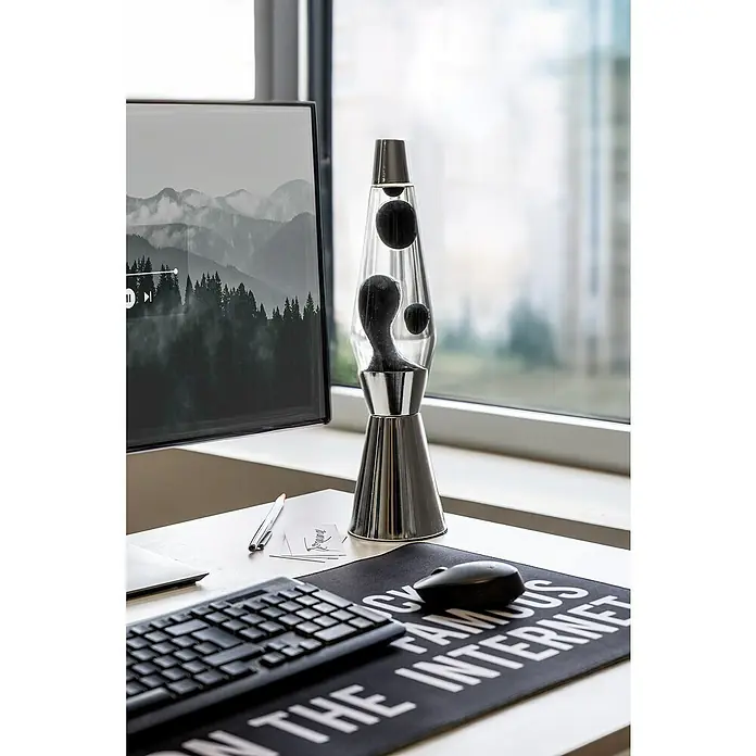 Lámpara de sobremesa decorativa de lava Bullet - 25 W, L x An x Al: 11,5 x 11,5 x 40 cm, Plata - La imagen muestra una lámpara de lava plateada sobre un escritorio junto a un ordenador. La lámpara añade un ambiente relajante al espacio de trabajo.