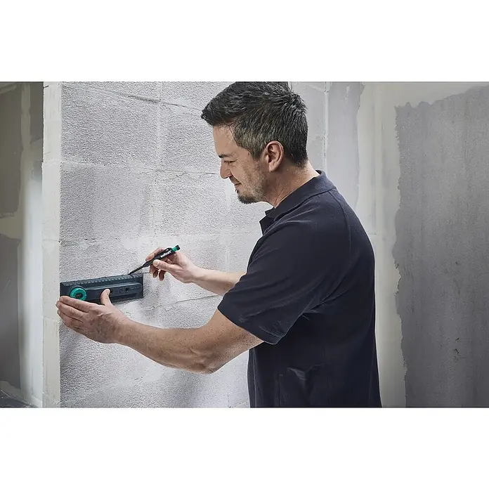Wolfcraft Plantilla de perforación - Específico para: Instalación de cajetines eléctricos en ladrillo - Hombre usando el Ángulo Universal Wolfcraft para realizar mediciones precisas en una pared, asegurándose de que todo esté perfectamente alineado.