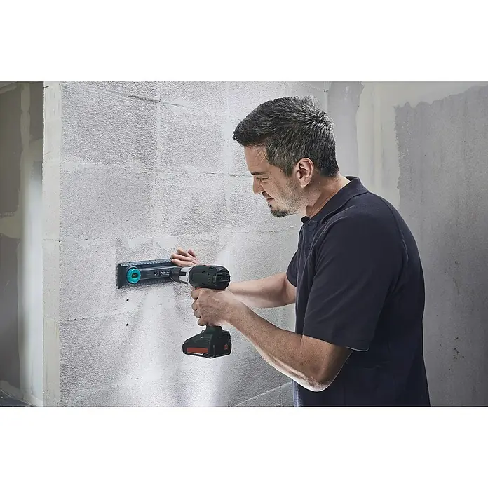 Wolfcraft Plantilla de perforación - Específico para: Instalación de cajetines eléctricos en ladrillo - Un hombre perfora una pared con un taladro inalámbrico y una plantilla para asegurar algo.