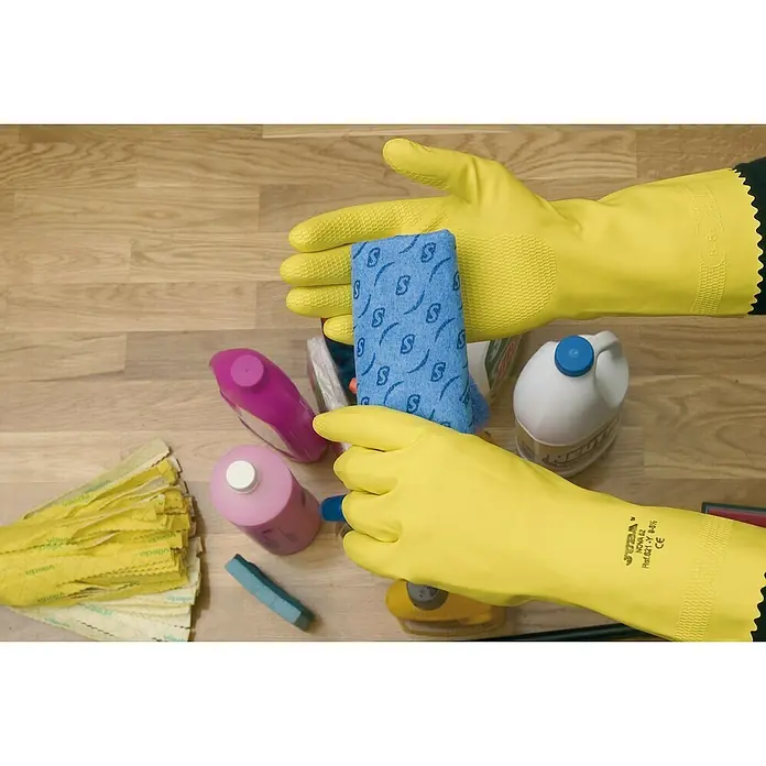 Juba Guantes de trabajo 621Y - Talla del guante: 10, Amarillo, 2 ud. - Guantes de goma amarillos sujetando un paño de limpieza azul, con botellas de líquido de limpieza y un cabezal de fregona amarillo en el suelo.