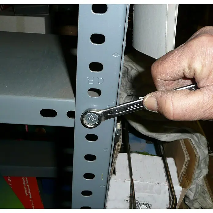 Juego de llaves combinadas - 8 pzs. - Primer plano de una mano apretando un perno en un estante metálico gris con una llave inglesa.