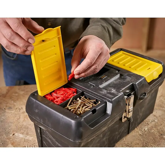 Stanley Caja para herramientas Millenium - L x An x Al: 41,1 x 18,5 x 19,9 cm, 16″, Plástico - Caja de herramientas de plástico con tapa amarilla, llena de tornillos y tacos, abierta por una mano.