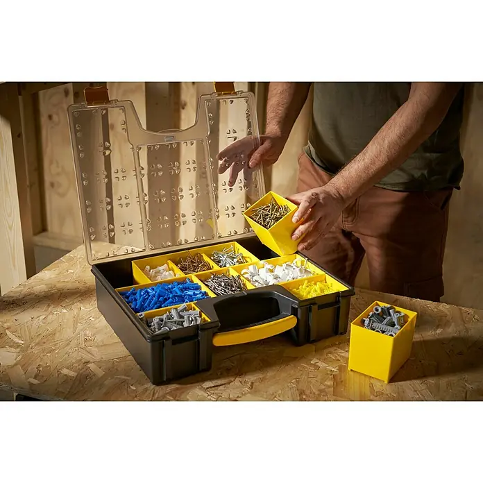 Stanley FatMax Estuche para piezas pequeñas 1-92-749 - Número de compartimentos: 8 ud., Profundo - Un hombre clasifica varios tornillos y tacos en una caja de herramientas negra con insertos amarillos.