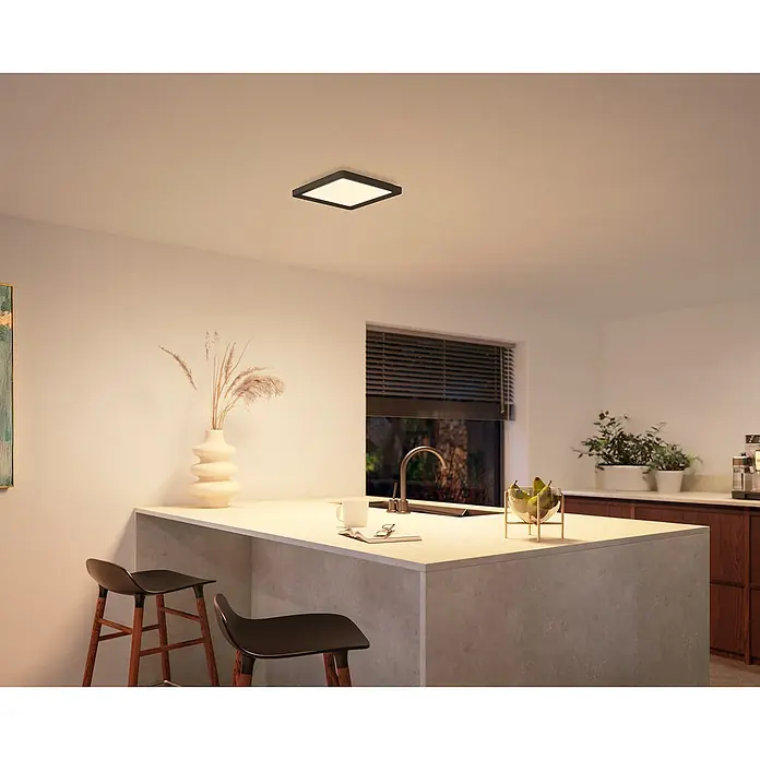 Philips Hue LED-Panel White Ambiance Tento S - 10,6 W, L x B x H: 29,5 x 29,5 x 3,5 cm, Schwarz, Kaltweiß - Eine moderne quadratische Deckenleuchte mit schwarzem Rahmen spendet warmes Licht in einer stilvollen Küche. Die Lampe hängt zentral über einer Kücheninsel.