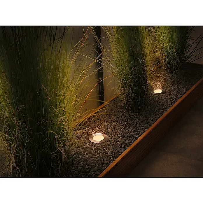 Paulmann Plug & Shine Basis-Set Floor insektenfreundlich - Anthrazit, IP67, Durchmesser: 9,8 cm, 3 Stk. - Garten-Szene mit eingelassenen Bodenleuchten, die in einer mit Kies gefüllten Pflanzbox installiert sind und dekoratives Licht auf Gräser werfen.