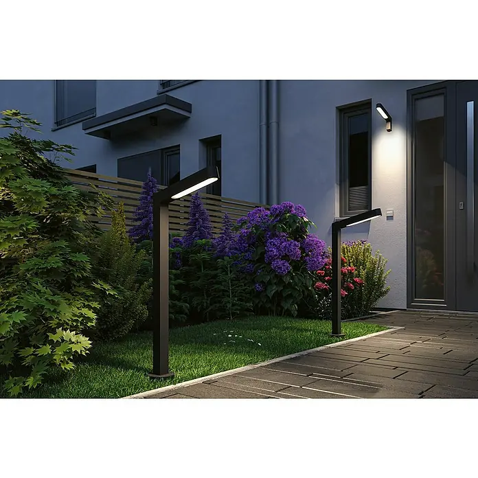 Paulmann Plug & Shine LED-Gartenspot Ito vertikal - 7,5 W, Warmweiß, L x B x H: 30 x 4,7 x 110 cm - Moderne Gartenbeleuchtung: Zwei schwarze Wegeleuchten beleuchten einen Gartenweg neben einem Haus mit üppiger Bepflanzung.