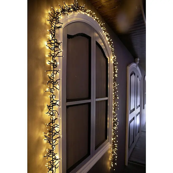 Tween Light Cadena de luces LED - Para exterior, Largo: 12,4 m, 1.000 ud., Funcionamiento en red - Una tira festiva de luces colgada alrededor de una ventana arqueada, creando un brillo cálido y acogedor.