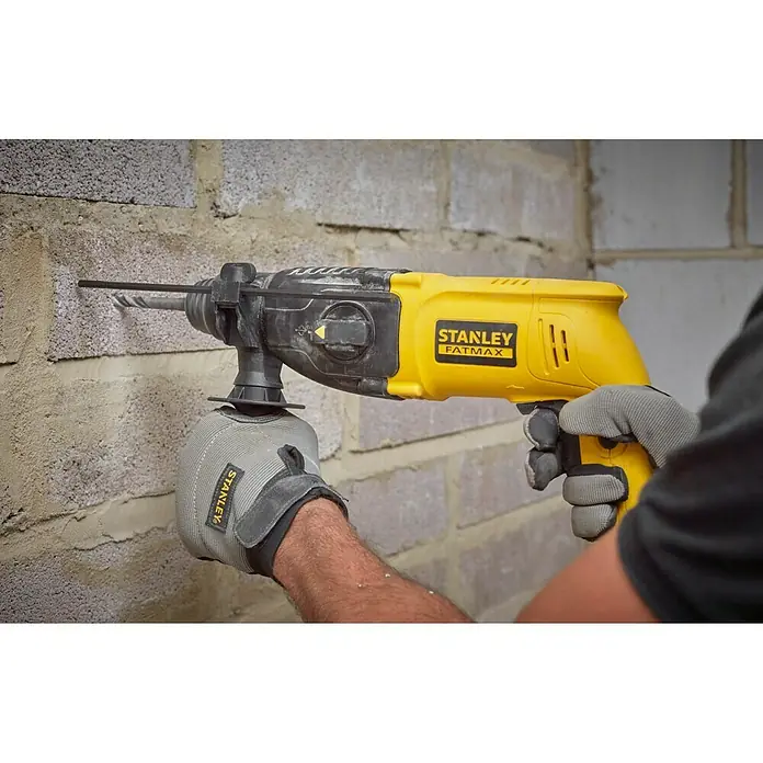 Stanley FatMax Martillo combinado SFMEH200K-QS - 750 W, 2,2 J, Alojamiento SDS-Plus - Primer plano de un taladro percutor Stanley Fatmax perforando una pared de ladrillo, sostenido por una persona con guantes de trabajo.