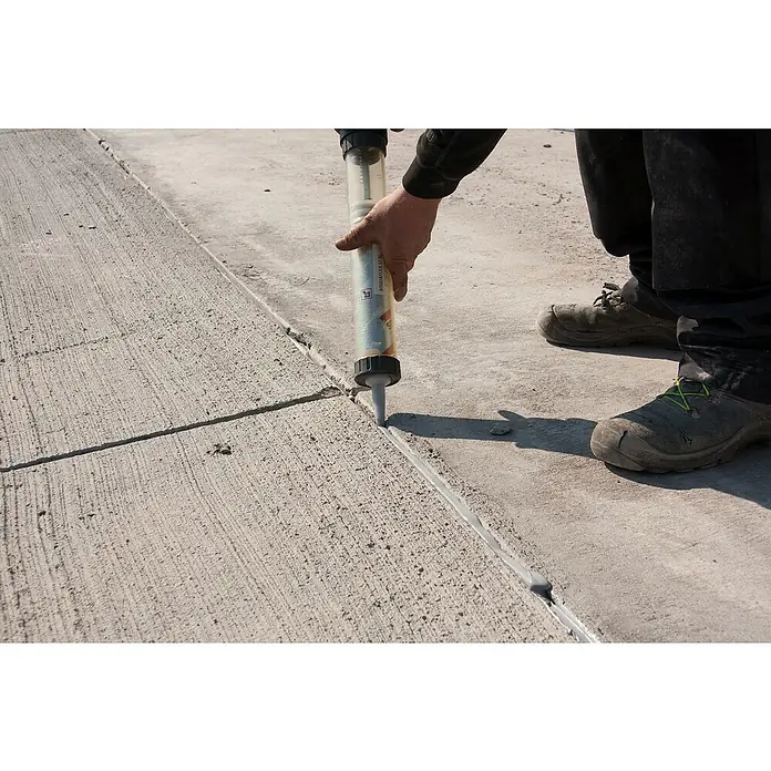 Soudal Pistola de silicona manual - Apto para: Silicona, 600 ml - Un trabajador de la construcción usa una pistola de calafateo para sellar una costura en el concreto.