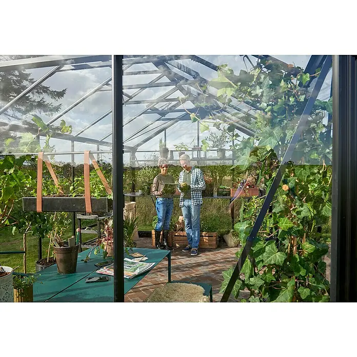 Juliana Gewächshaus Jubii 60 - Material Seitenwand: Glas, 3 mm, Schwarz - Ein Gewächshaus mit einem Tisch voller Gartengeräte und zwei Personen im Hintergrund, die sich einen Gartenplan ansehen.