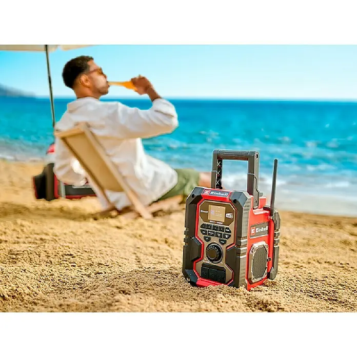 Einhell Power X-Change 18V Akku-Baustellenradio TE-CR 18 Li DAB+/FM/BT - Solo - 18 V, Ohne Akku, Bluetooth - Ein rotes und schwarzes Einhell Baustellenradio steht am Strand, im Hintergrund ein Mann mit Getränk und Meer.