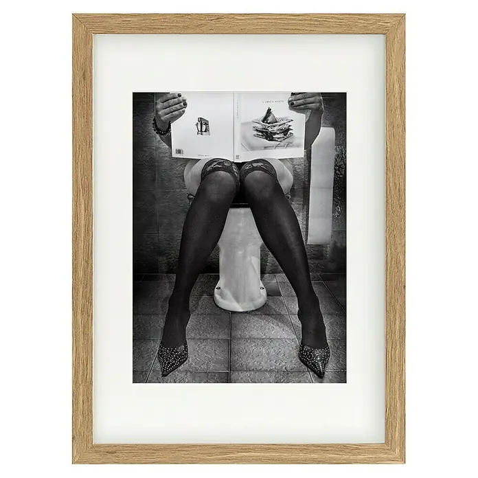 Papermoon Bild - Le Goart des Autres, B x H: 40 x 50 cm, Mit Passepartout, Rahmen Eiche - Gerahmtes Schwarz-Weiß-Foto einer Frau auf der Toilette, die ein Kochbuch liest, mit Fokus auf Stockings und Schuhen.