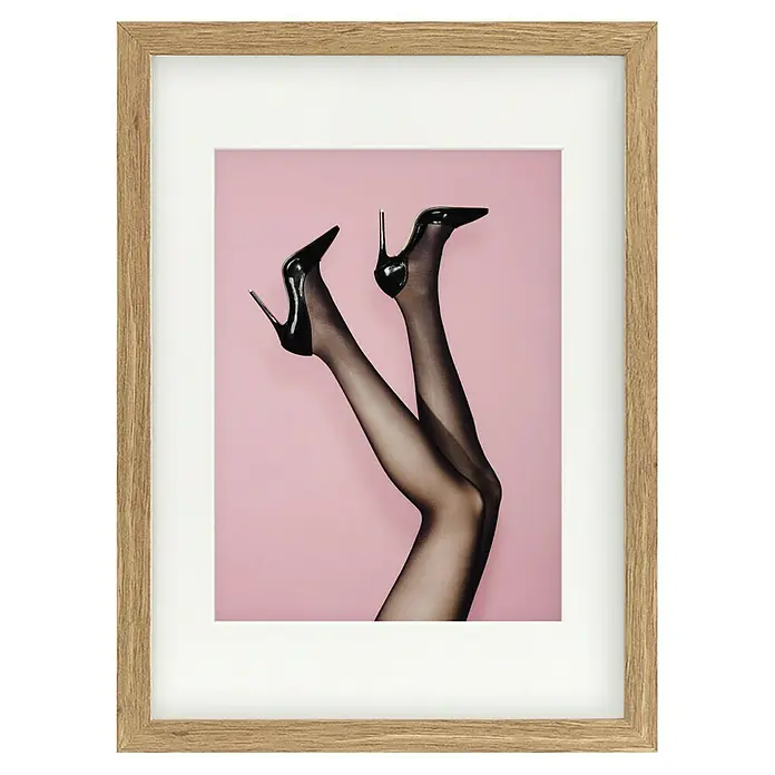 Papermoon Bild - Kick up your Heels, B x H: 70 x 100 cm, Mit Passepartout, Rahmen Eiche - Gerahmtes Bild mit einem pinkfarbenen Hintergrund, auf dem ein Paar Beine mit schwarzen Strümpfen und High Heels zu sehen sind.