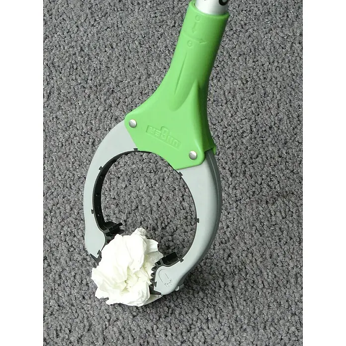Unger Greifzange Nifty Nabber - Länge: 92 cm - Eine Greifzange mit grünen und grauen Akzenten hält ein zerknittertes weißes Papiertuch vor einem grauen Teppichhintergrund.