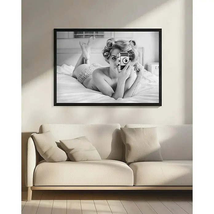 Papermoon Bild - A Chick, B x H: 80 x 60 cm, Mit Passepartout, Rahmen Schwarz - Schwarzweißbild einer Frau mit Lockenwicklern und Kamera über einem hellen Sofa, gerahmt.