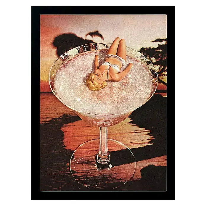 Papermoon Bild - Pink Margarita, B x H: 80 x 110 cm, Ohne Passepartout, Rahmen Schwarz - Martini-Glas mit Glitzerfüllung und einer Miniaturfigur einer Frau im Bikini, vor einem verschwommenen Strandhintergrund.