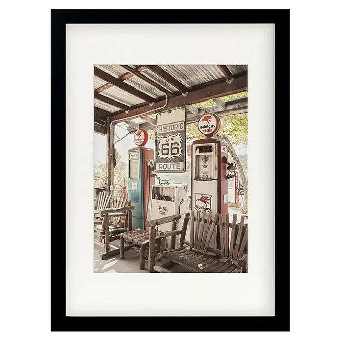 Papermoon Bild - Route 66 Gas Station, B x H: 50 x 70 cm, Mit Passepartout, Rahmen Schwarz - Gerahmtes Foto einer nostalgischen Tankstelle mit Route 66 Schild, alten Zapfsäulen und rustikalen Holzstühlen, die Vintage-Atmosphäre versprühen.