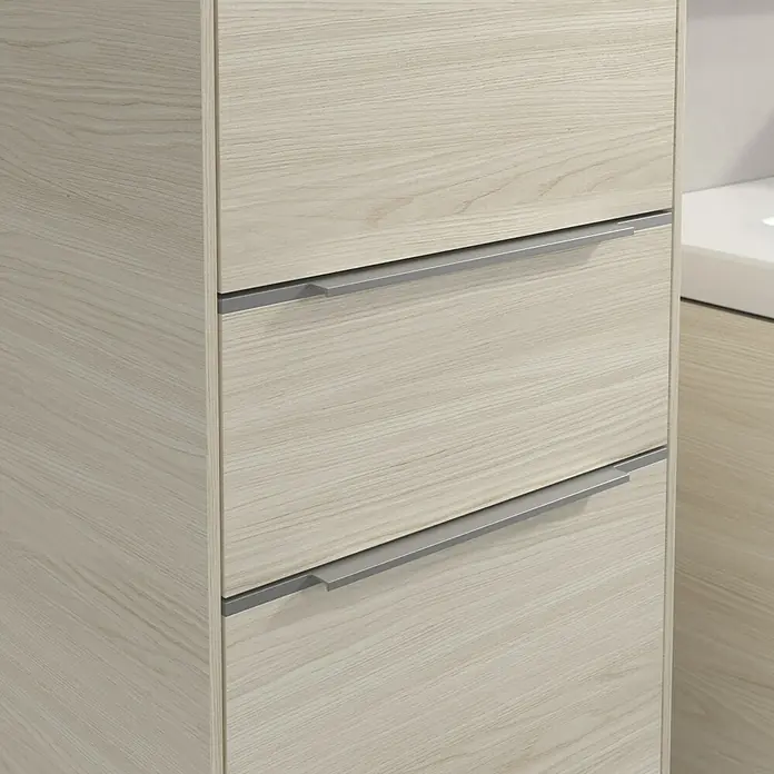 Villeroy & Boch Subway 3.0 Hochschrank - B x T x H: 40 x 36,2 x 171 cm, 1x Schublade, 2x Tür, White Oak, Farbe Griff: Aluminium glänzend, DIN Anschlag: Links - Nahaufnahme eines hellen Holzschranks mit drei Schubladen und silbernen Griffen, der ein modernes Möbelstück im Detail zeigt.