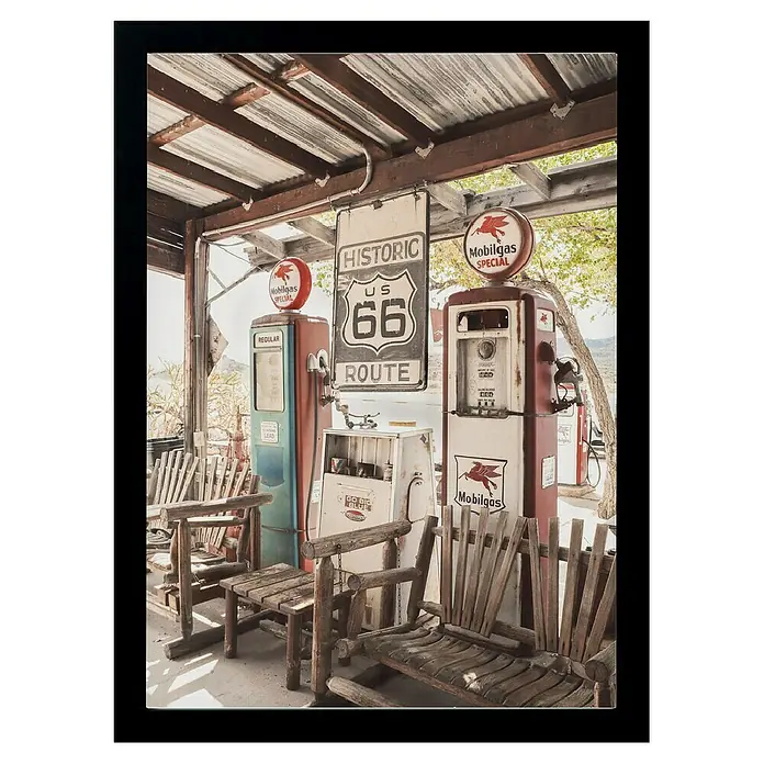 Papermoon Bild - Route 66 Gas Station, B x H: 70 x 100 cm, Ohne Passepartout, Rahmen Schwarz - Nostalgische Aufnahme von alten Zapfsäulen und einer Route 66-Beschilderung, umgeben von rustikalen Holzmöbeln.
