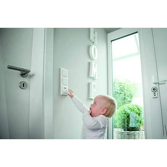 Abus Steckdosenschutz Greta - Weiß, 6 Stk. - Kind erreicht Steckdose mit integrierten Schaltern an der Wand, umgeben von Türen und Dekorationsbuchstaben, die das Wort "HOME" bilden.