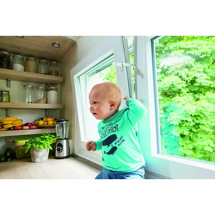 Abus Fenstersicherung NinoWeiß - Bild einer Fenstersicherung, montiert an einem Fenster, mit einem Baby im Vordergrund, das sich in der Küche befindet.
