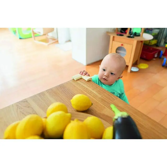 Abus Eckenschutz Jannic - 4 Stk., Beige - Ein Baby steht an einem Tisch voller Zitronen und einer Aubergine, neugierig auf die sauren und bitteren Köstlichkeiten.