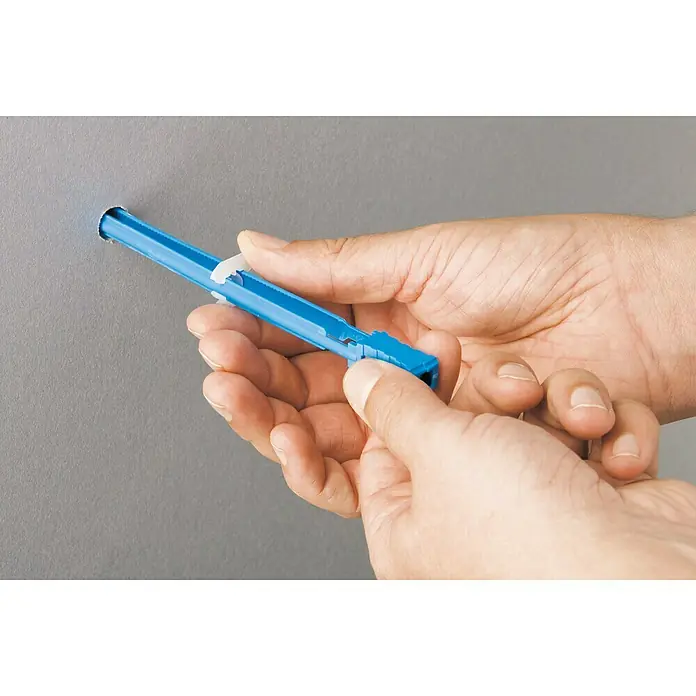 Knauf Gipsplatten Klappdübel Hartmut - Länge Dübel: 190 mm, Länge Schraube: 60 mm - Nahaufnahme von Händen, die einen blauen Hohlraumdübel in eine graue Wand einführen.
